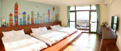 A hotel room with two beds, a TV, a balcony with a view, and a colorful cityscape mural on the wall.