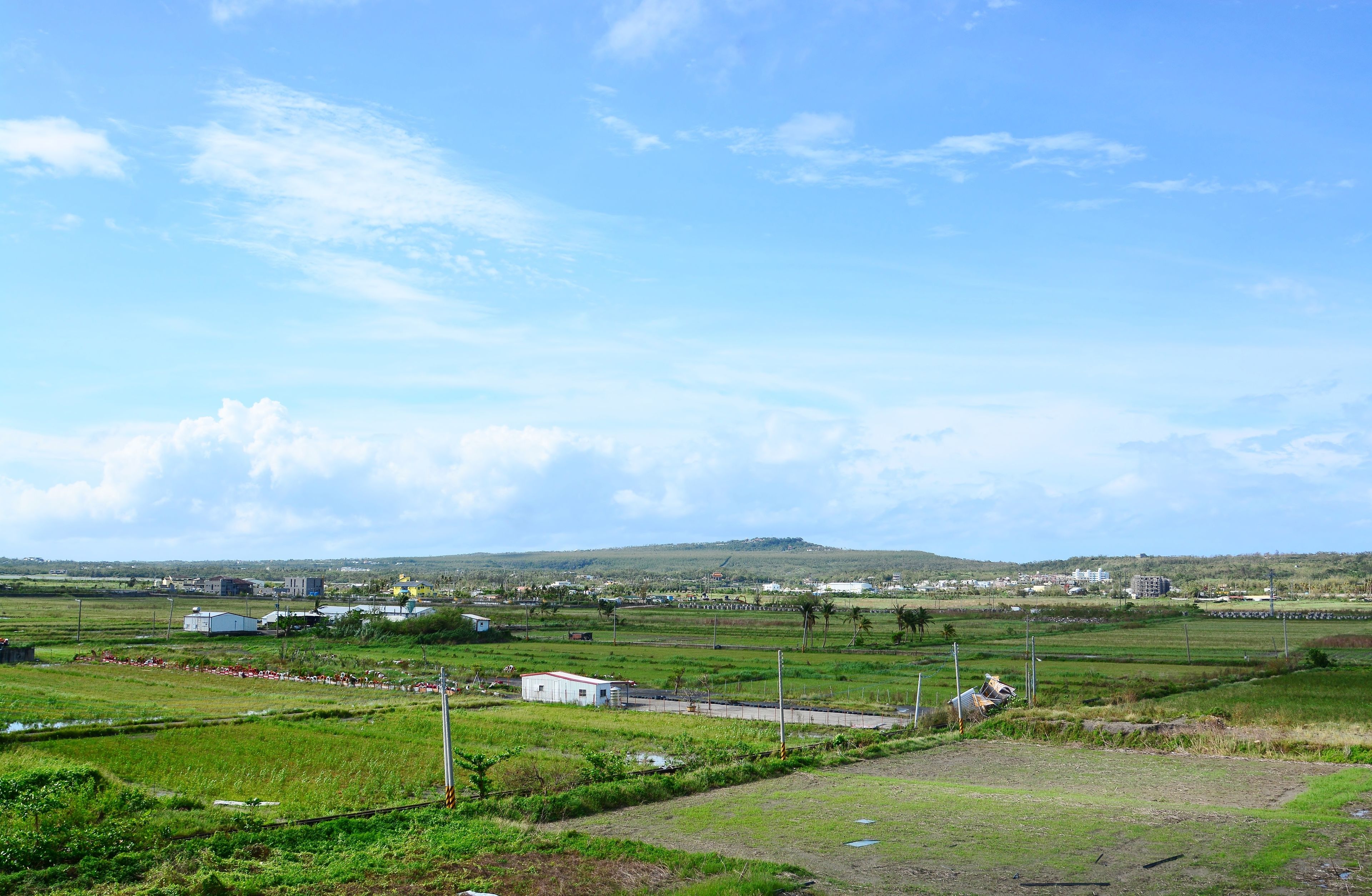 A rural landscape with fields, a small building, and distant hills.