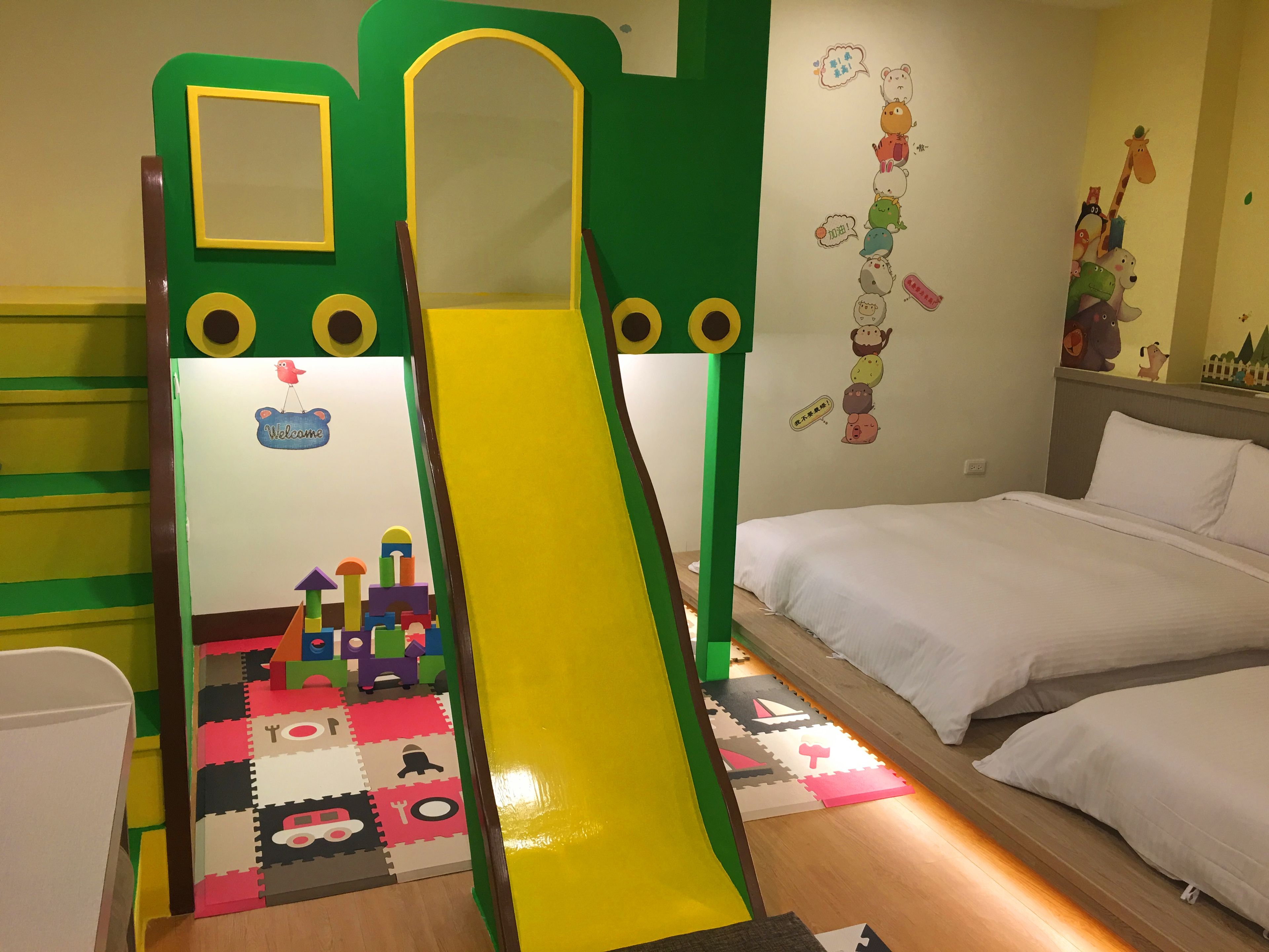 Ein Spielbereich für Kinder mit Rutsche, bunten Spielmatten und einem Bett mit weißer Bettwäsche.