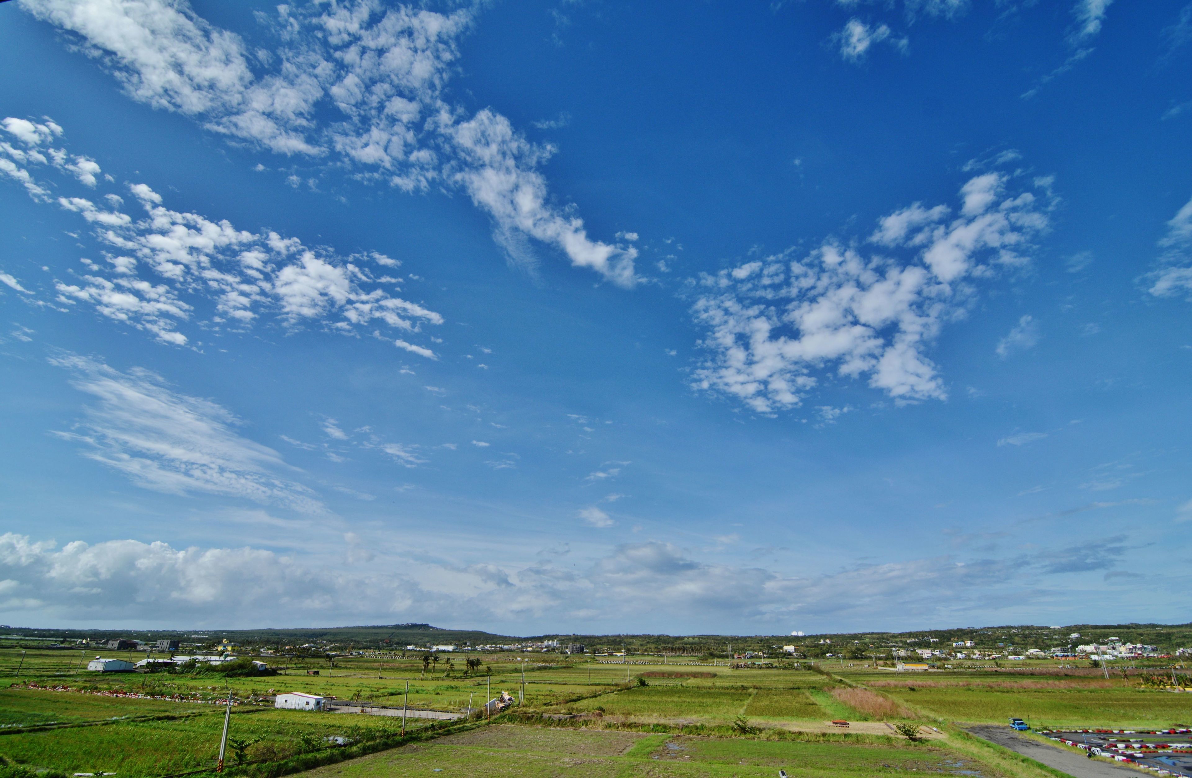 A rural landscape with fields, a few buildings, and a clear blue sky.