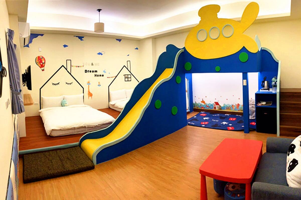 A children's play area with a slide, two beds, a sofa, and a small table.
