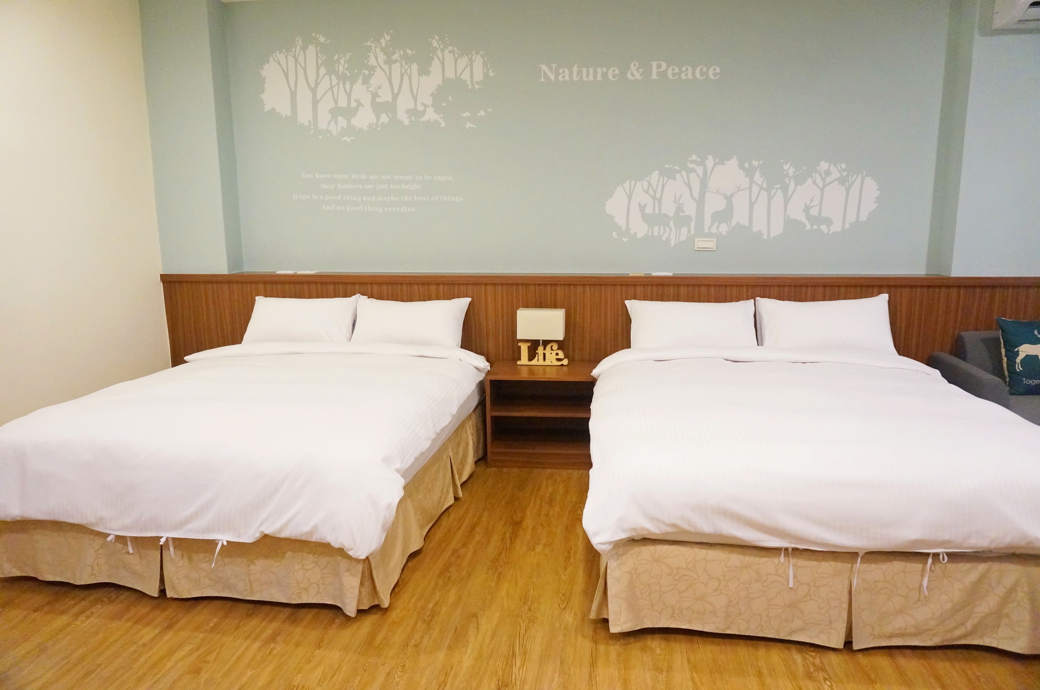 A hotel room with two beds, a nightstand, and a wall mural depicting nature and peace.