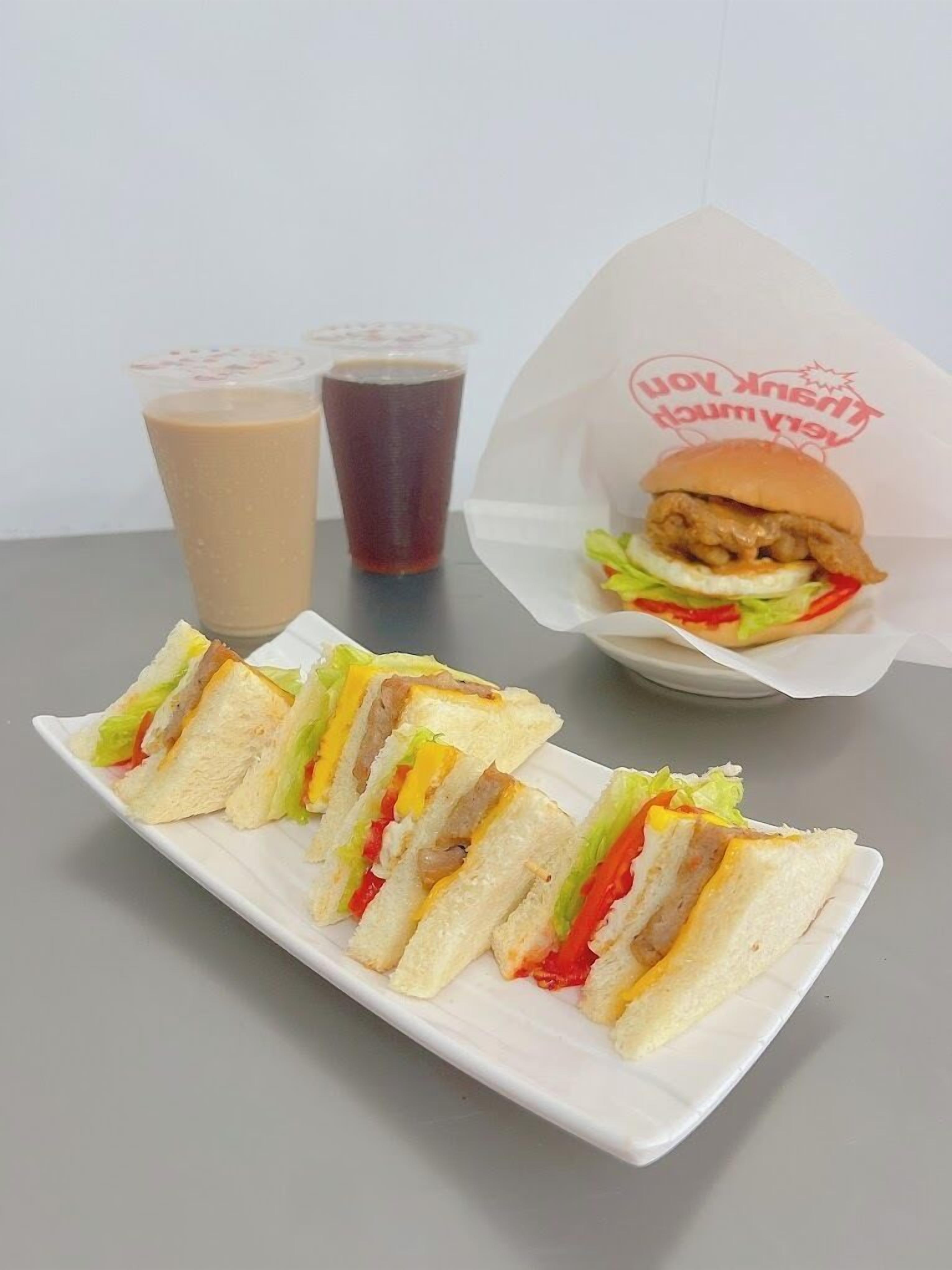 A sandwich with lettuce, tomato, and cheese, a drink in a cup, and a burger in a wrapper.