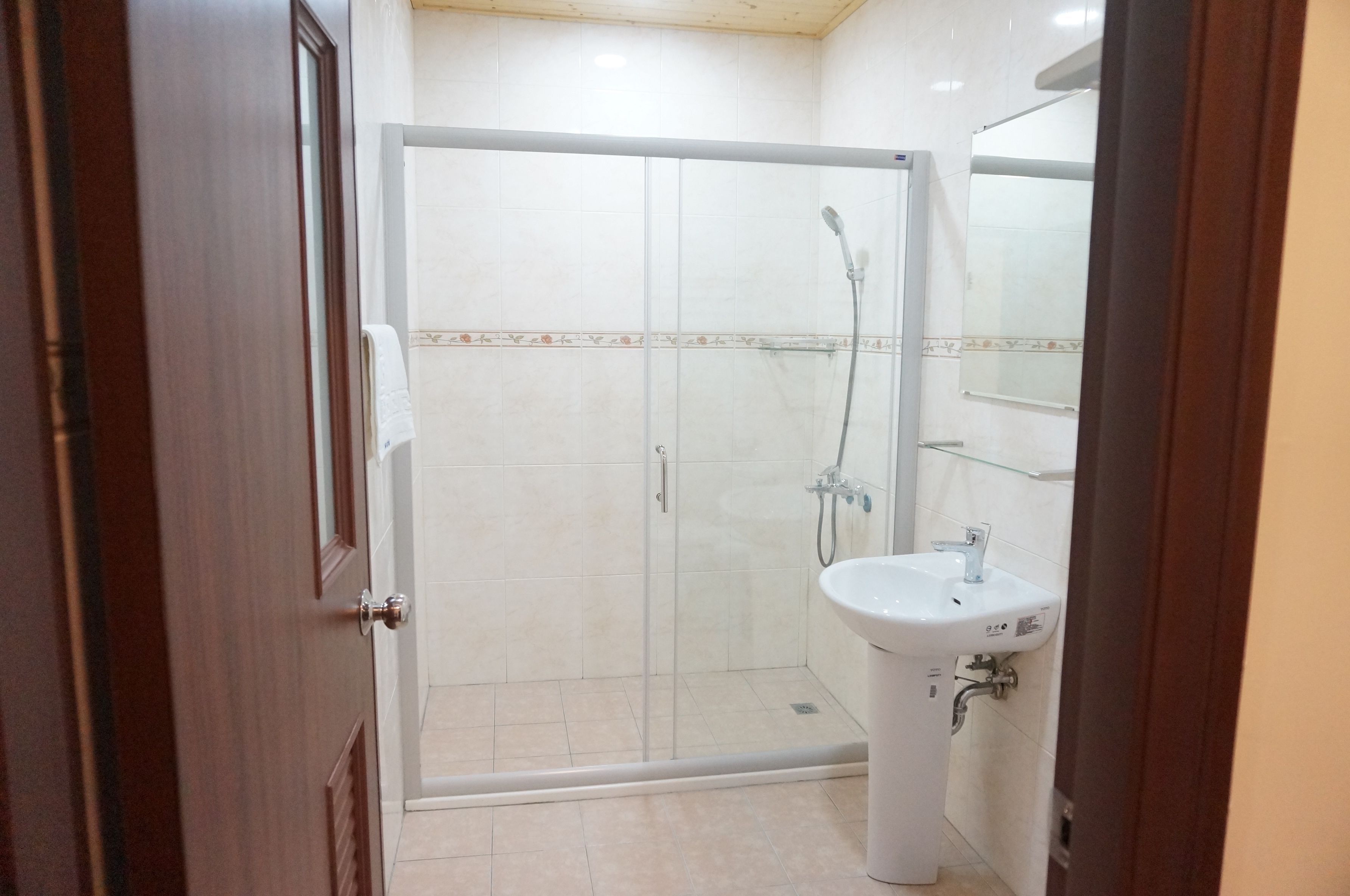 Un baño con ducha de vidrio, un lavabo blanco y un espejo sobre el lavabo.