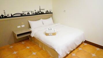 A hotel room with a bed, a small bedside table, a wall decoration with city names, and a tiled floor.