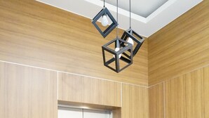 Un ascensor con detalles metálicos, paneles de madera y una lámpara moderna de diseño geométrico.