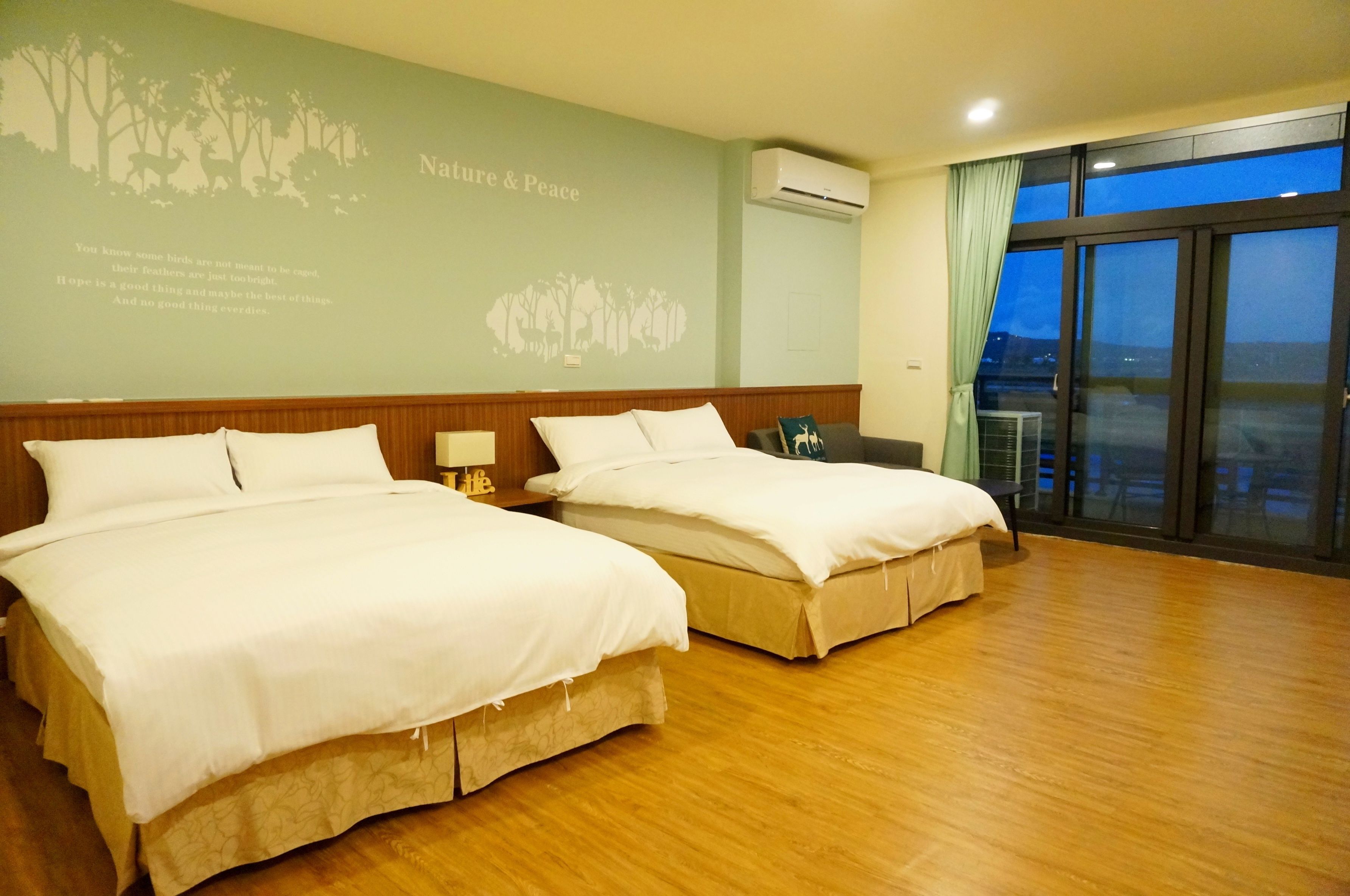 Habitación de hotel con dos camas, piso de madera, un ventanal con vistas y un mural temático de naturaleza.