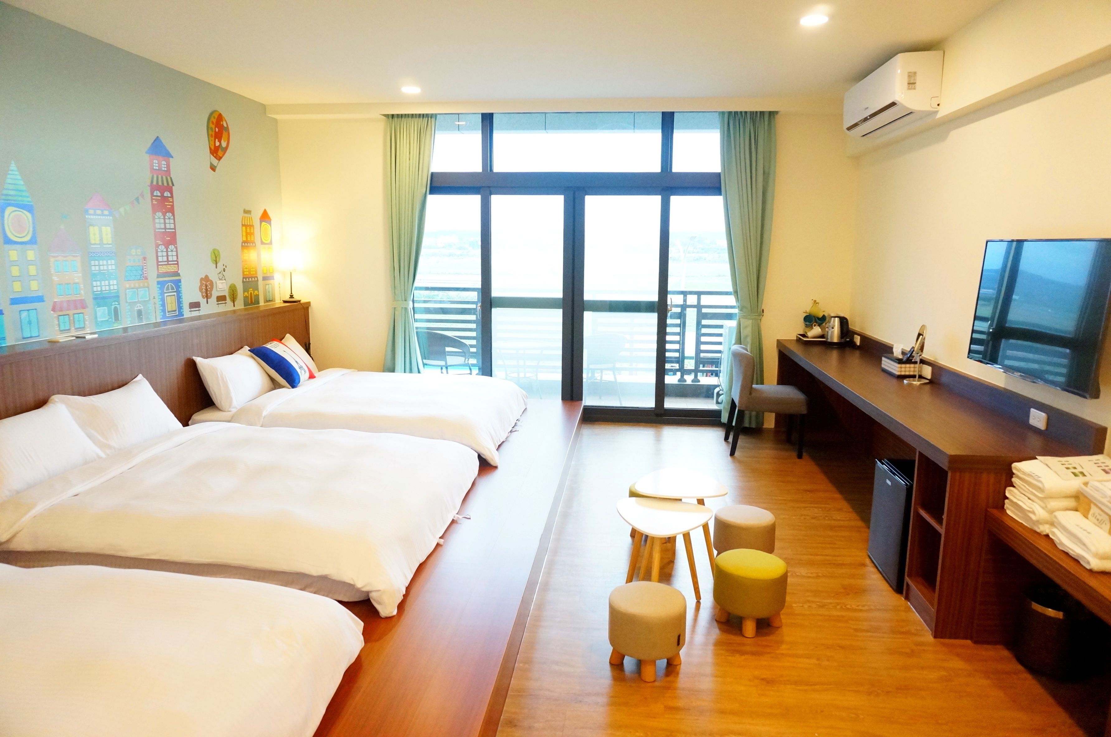 A hotel room with two beds, a desk, a TV, and a balcony with a view.
