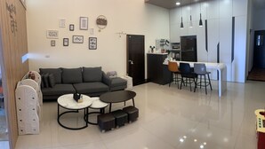 Una sala de estar moderna con un sofá gris, dos mesas redondas y una zona de cocina con taburetes de bar.