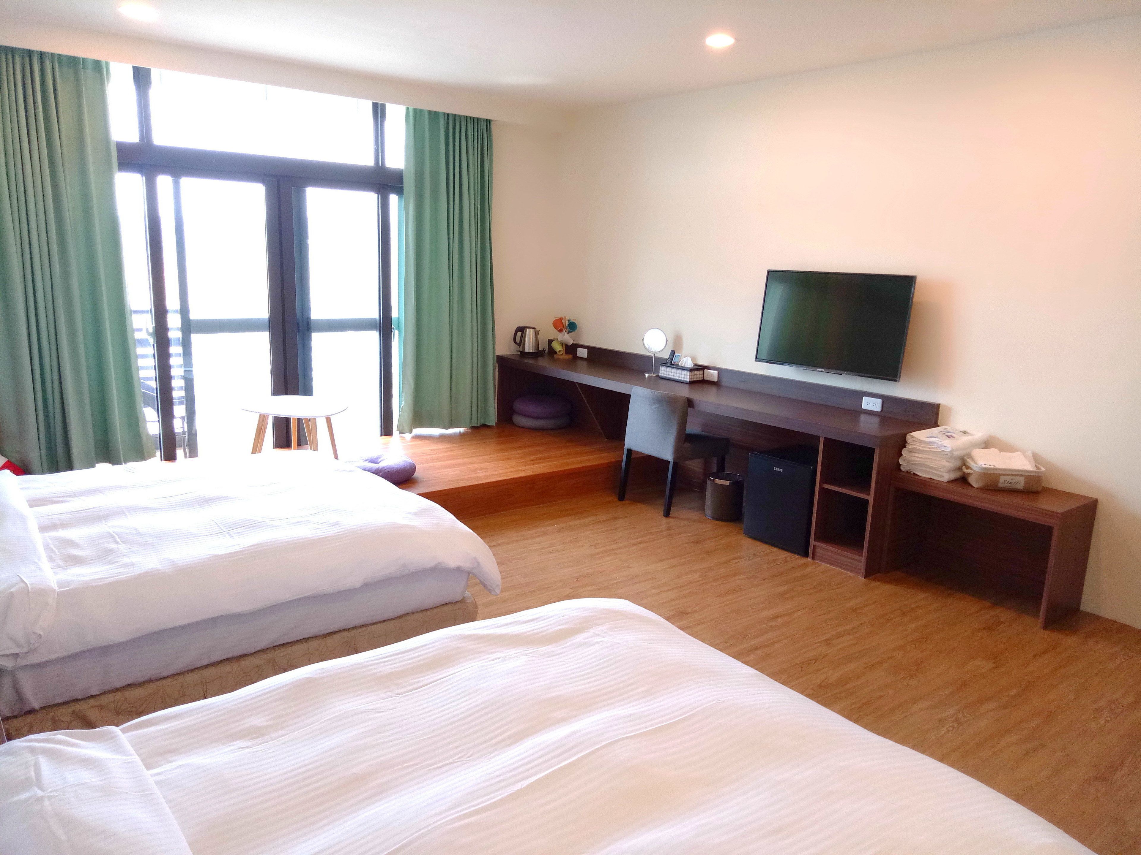 A hotel room with two beds, a desk, a television, and a window with curtains.