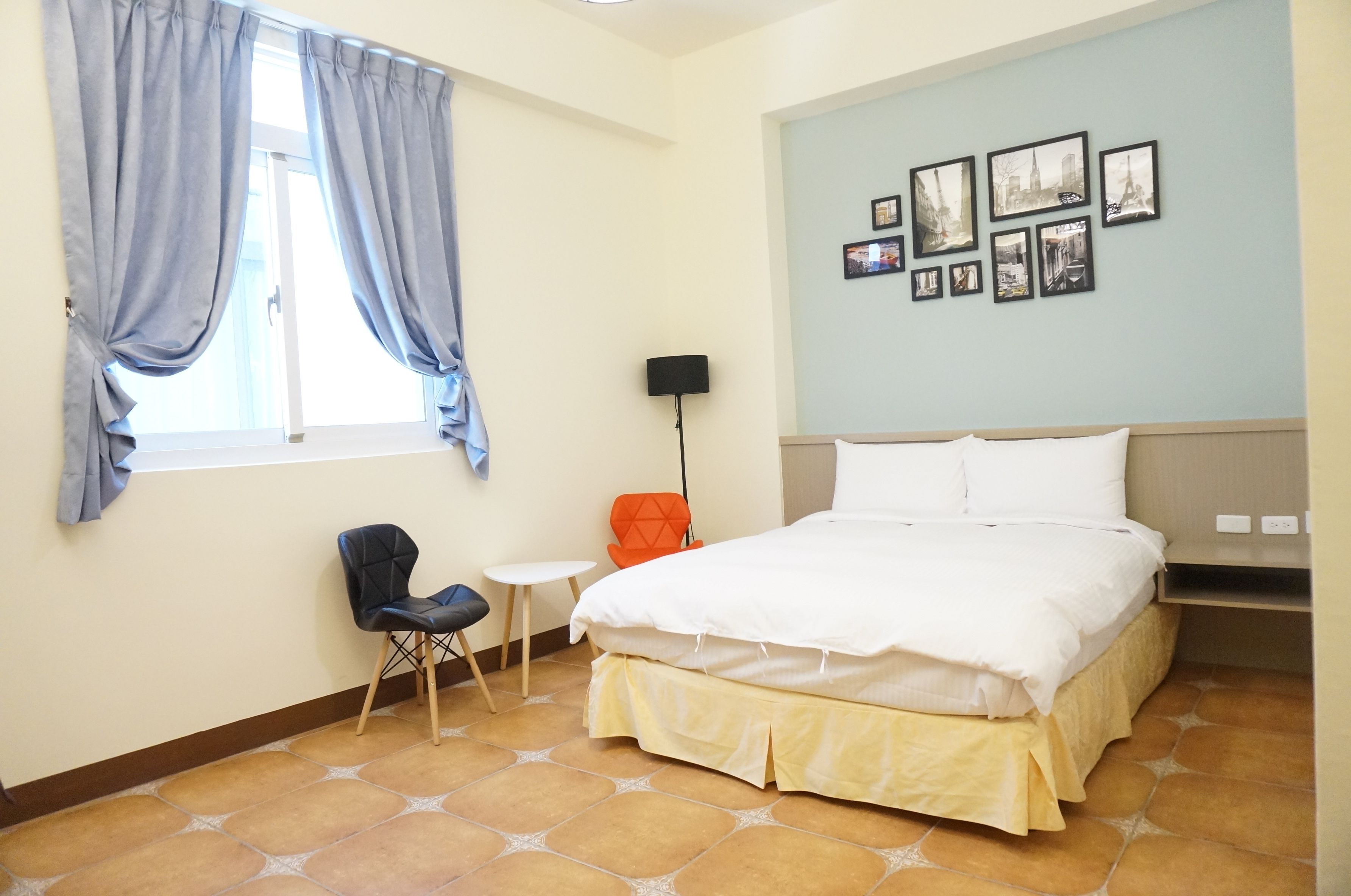 A hotel room with a bed, a chair, a small table, a lamp, and a window with curtains.