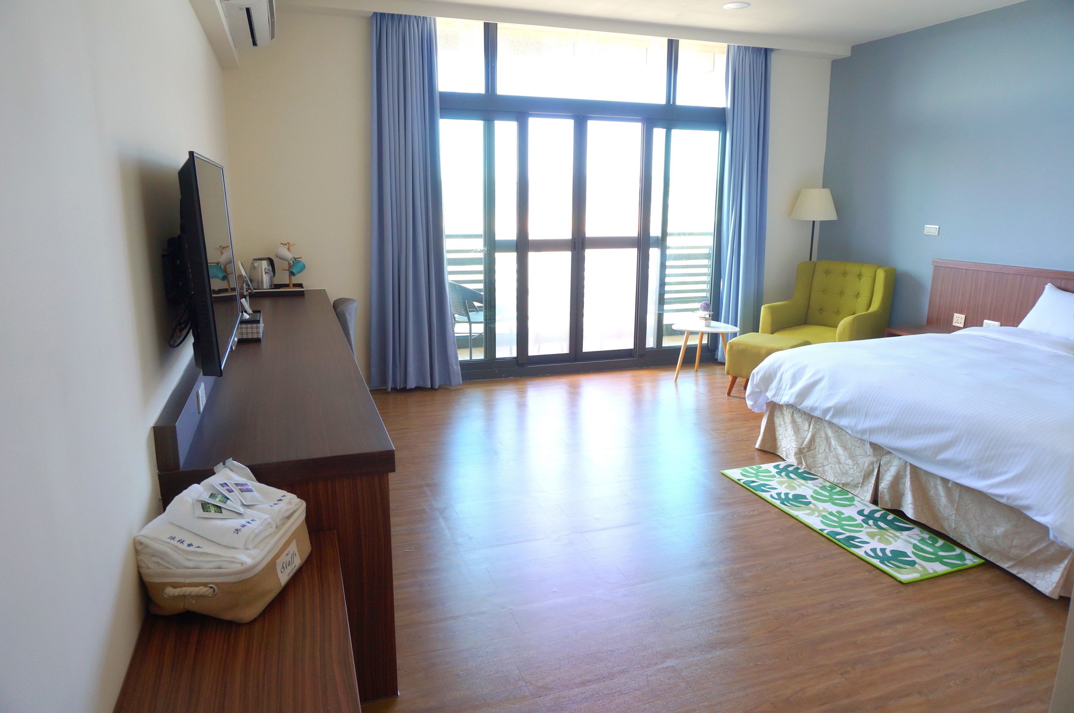 Habitación de hotel con cama, escritorio con computadora, una silla y ventana con cortinas.