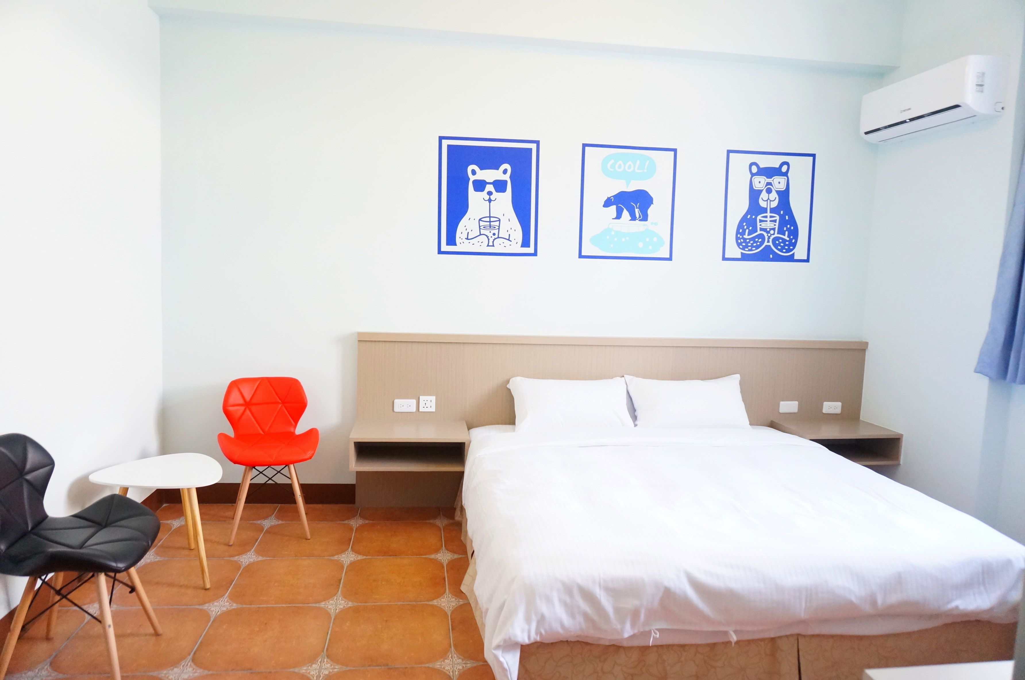 Une chambre d’hôtel comprenant un lit, une petite table, deux chaises et trois œuvres d’art murales.
