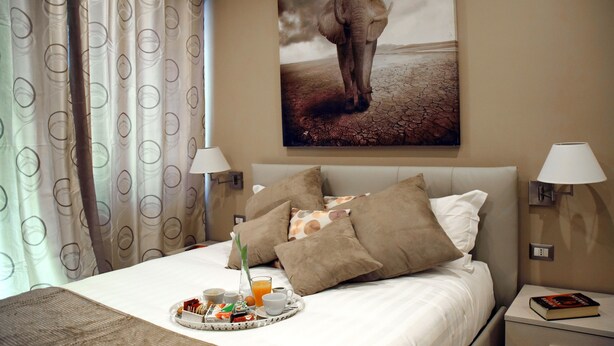 A hotel room with a bed, pillows, a tray with breakfast, a lamp, and a painting of an elephant. - Gregori Guest House (Rome)