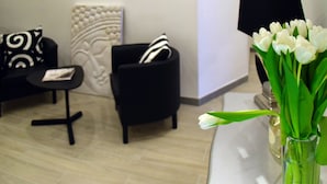 A modern living room with a black sofa, a white accent wall, and a vase of white tulips on a table. - Gregori Guest House (Rome)