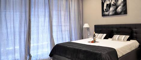A bedroom with a large bed, a headboard, a bedside table with a lamp, and a painting on the wall.
