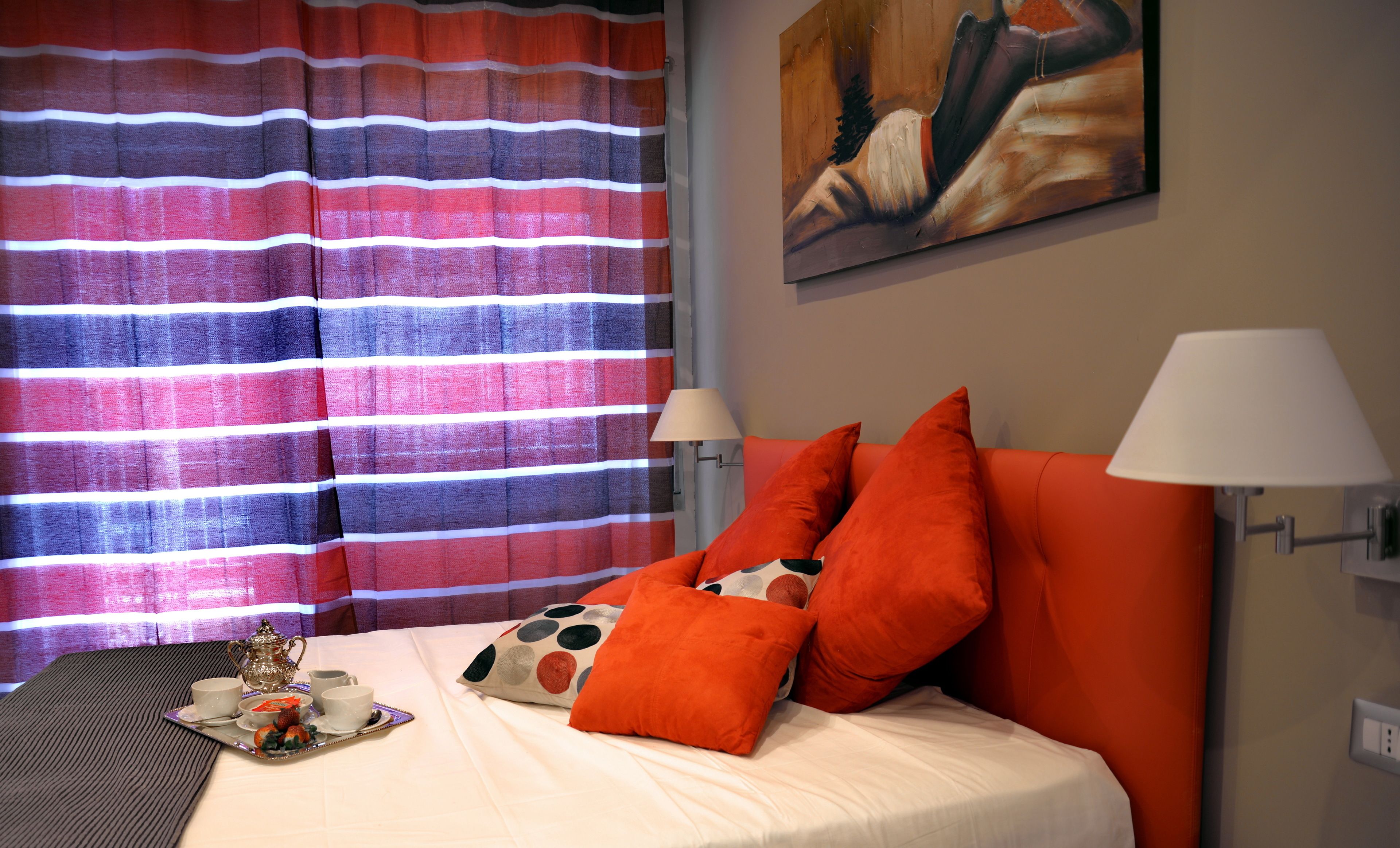 Una cama bien hecha con ropa blanca, dos almohadas naranjas y una bandeja con juego de té.