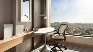 Habitación de hotel moderna con vista a la ciudad, una mesa redonda, un escritorio, una silla y una lámpara.
