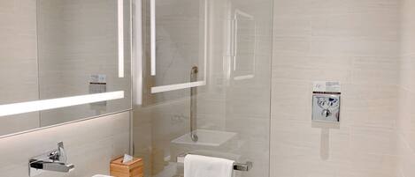 Un baño moderno con ducha de vidrio, un lavabo blanco y un espejo sobre él.