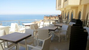Una terraza con mobiliario de mimbre, vista al mar y un edificio con ventanas arqueadas.