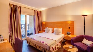 Habitación de hotel con cama, escritorio, silla, sofá púrpura y balcón con cortinas.