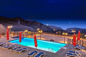 A pool area with lounge chairs and umbrellas, surrounded by a wooden fence, under a night sky. - El Jabal Sokhna Hotel (Ataqah)
