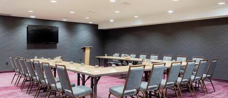 A conference room with a long table, multiple chairs, a podium, and a flat-screen TV on the wall.