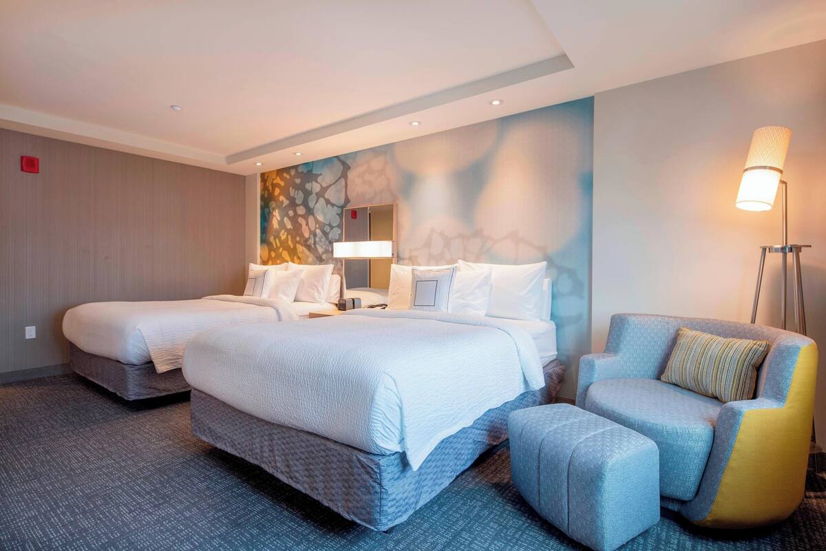 A hotel room with two beds, a sofa, a lamp, and a wall with a decorative pattern.