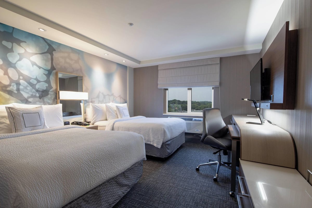A hotel room with two beds, a desk, a chair, a TV, and a window with a view.