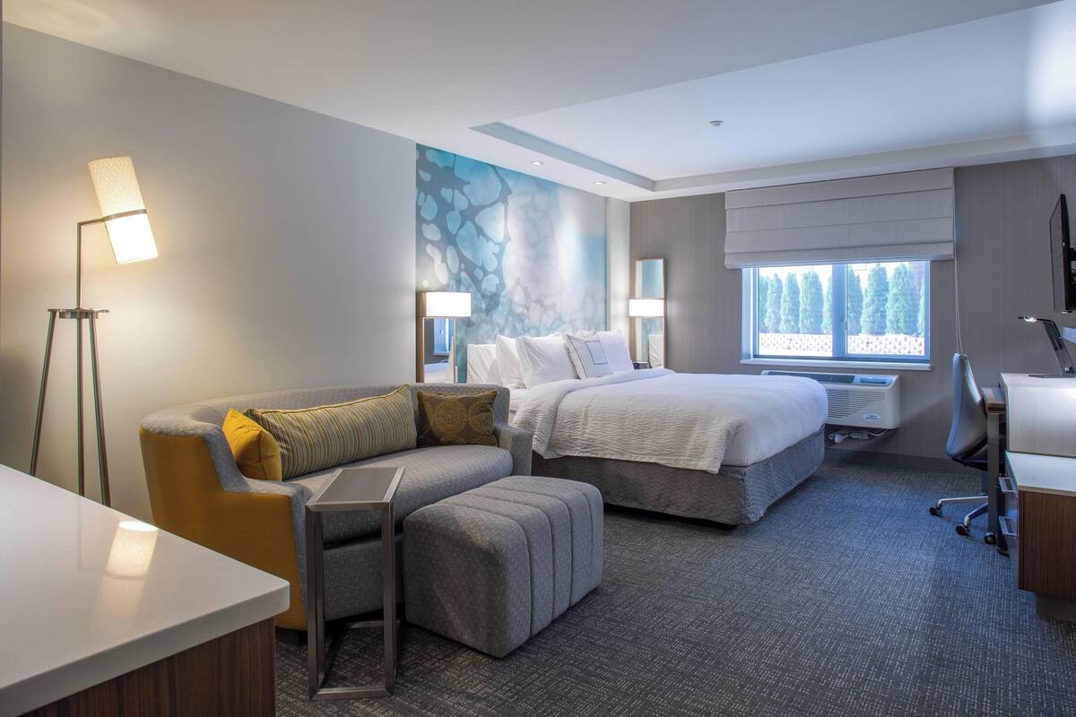 A hotel room with a bed, a sofa, a desk, and a standing lamp.