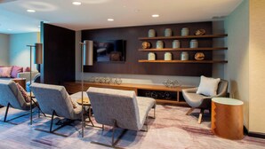 A modern living room with a sofa set, a coffee table, and a TV mounted on the wall. There are shelves with decorative items and a wooden console table. - Courtyard by Marriott New York Queens/Fresh Meadows (Fresh Meadows)