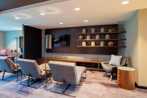 Una sala de estar moderna con un conjunto de sofá, una mesita de centro y un televisor montado en la pared. Hay estanterías con objetos decorativos y una consola de madera.
