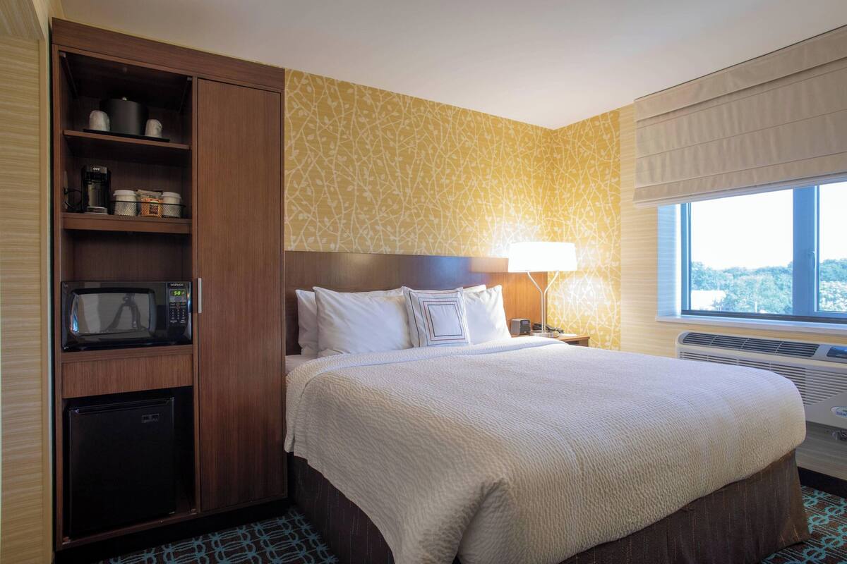 A hotel room with a large bed, a wardrobe, a microwave, a mini-fridge, and a window with a view.