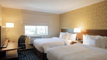 Ein Hotelzimmer mit zwei Betten, einem Schreibtisch, einem Stuhl, einer Lampe und einem Fenster.