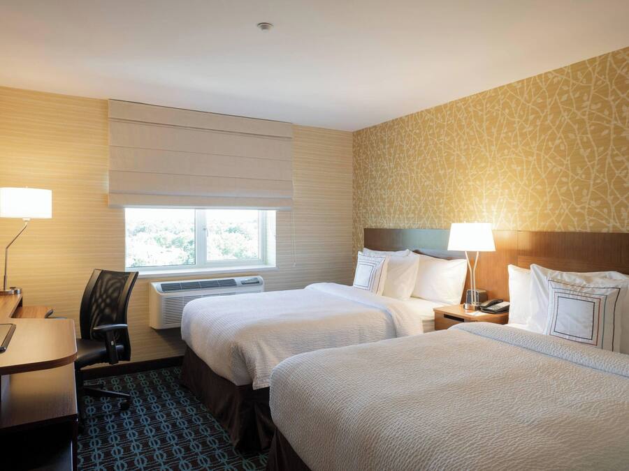 Ein Hotelzimmer mit zwei Betten, einem Schreibtisch, einem Stuhl, einer Lampe und einem Fenster.