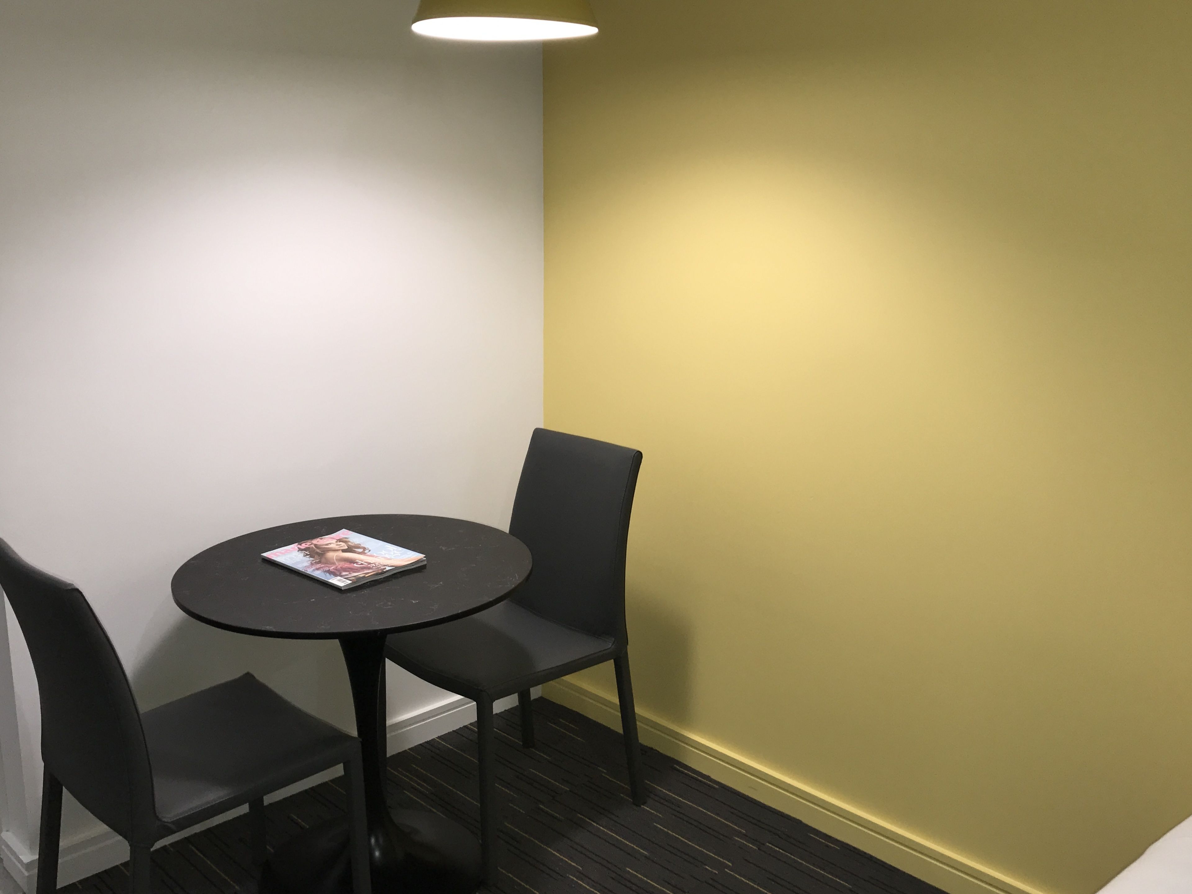 A small, round table with a magazine, two black chairs, and a light fixture above.