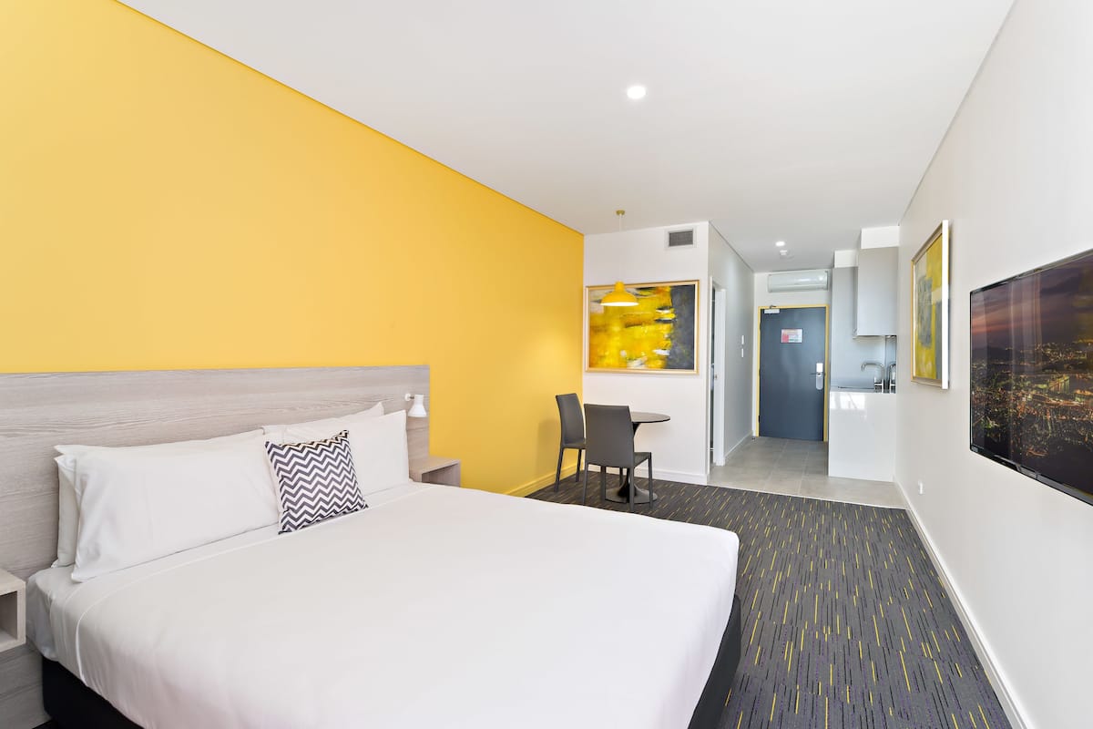 Ein Hotelzimmer mit einem großen Bett, einem Schreibtisch und einem Sessel. Im Hintergrund ist ein Badezimmer zu sehen.