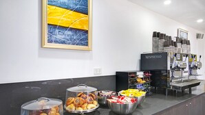Un buffet de petit-déjeuner proposant diverses pâtisseries, une machine à café et une œuvre d’art encadrée au mur.