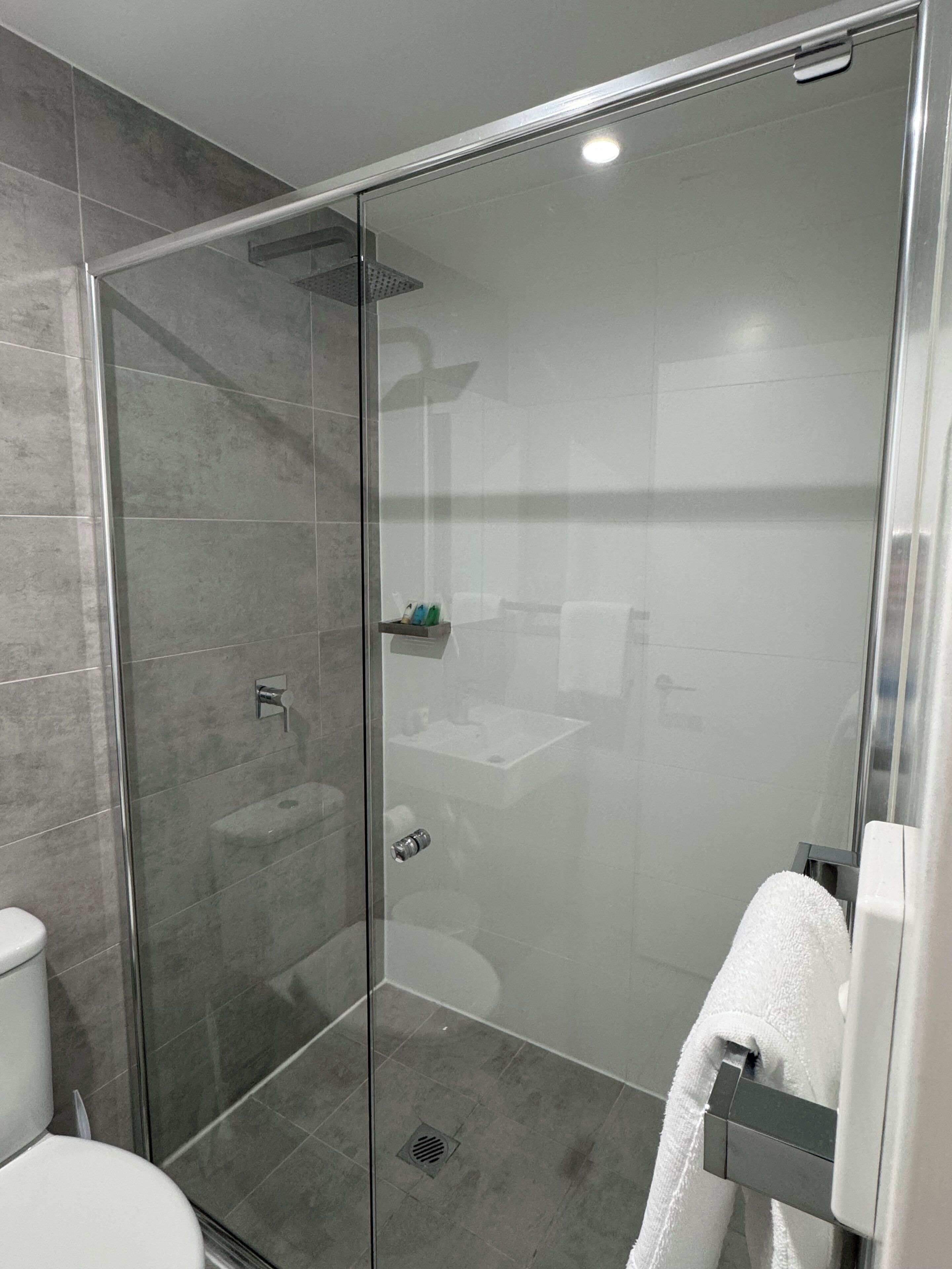 Un baño moderno con ducha envuelta en vidrio, inodoro y lavabo con toallero.