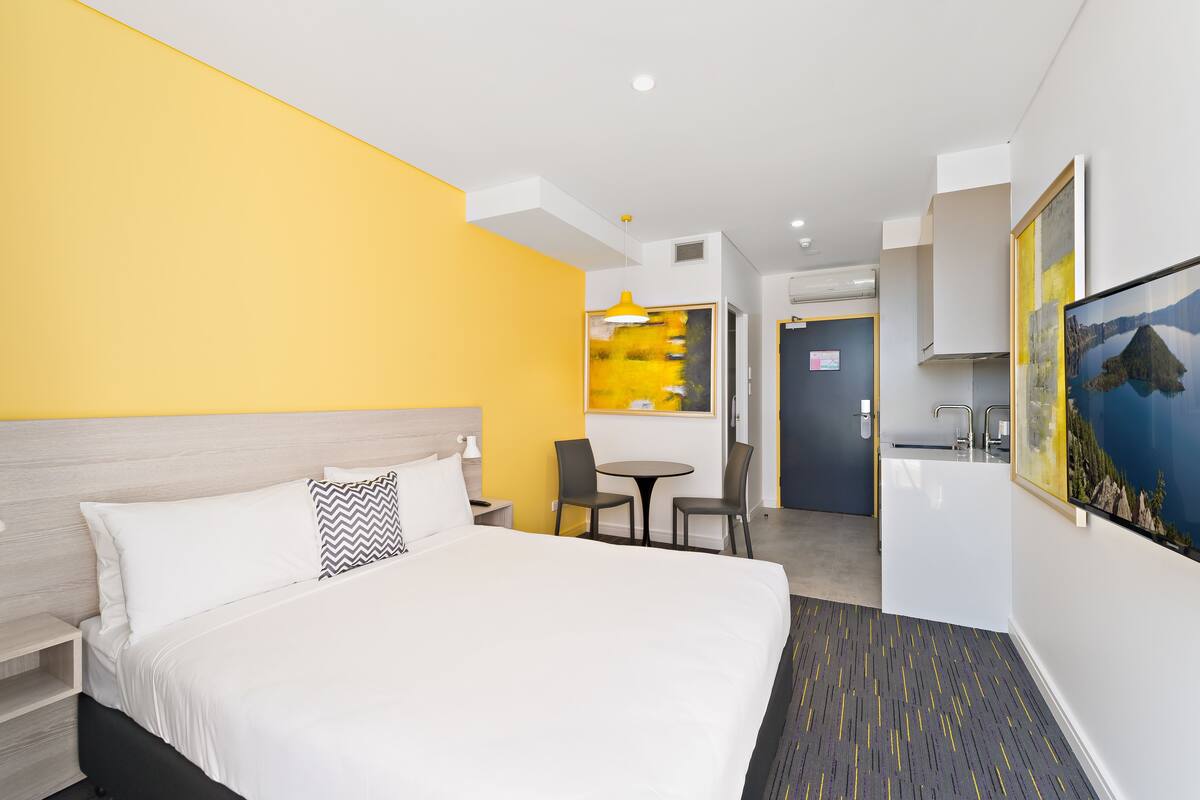 Ein Hotelzimmer mit einem Bett, einem Schreibtisch und Stühlen. An der Wand hängt ein Gemälde und das Fenster bietet einen Ausblick.