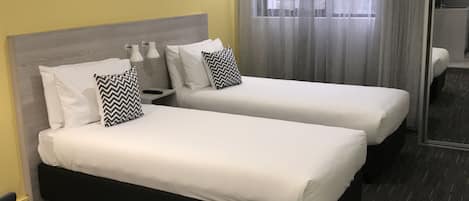 Una habitación de hotel con dos camas individuales, una mesita de noche con lámpara y un espejo grande.