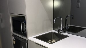 Une cuisine moderne équipée d’appareils électroménagers en acier inoxydable, d’un évier à deux bacs et d’un micro-ondes compact.