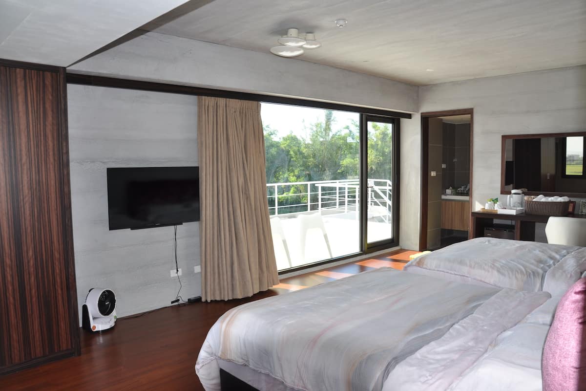 Quarto de hotel moderno com uma cama grande, televisão de tela plana na parede, ventilador de teto e porta de vidro deslizante para área externa.