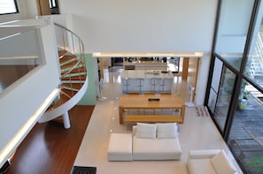 Ein modernes Interieur mit einer zentralen Sitzecke, einer Küche im Hintergrund und einer Wendeltreppe.