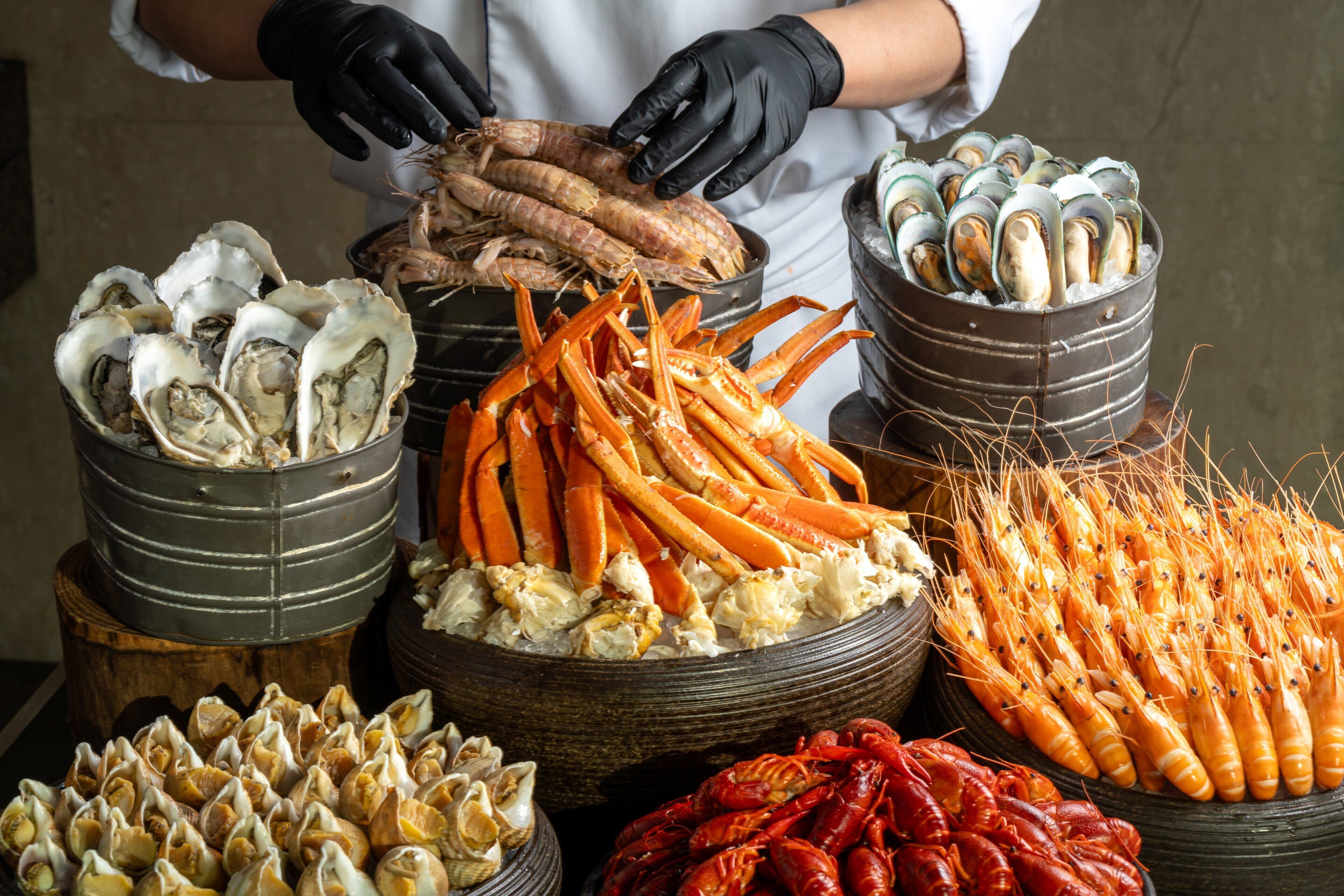Une variété de fruits de mer, notamment des huîtres, des pinces de crabe et des crevettes, présentés dans des récipients en métal.