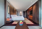 A modern hotel room with a large bed, a bedside table with a lamp, a TV, and a fruit bowl on a small table.