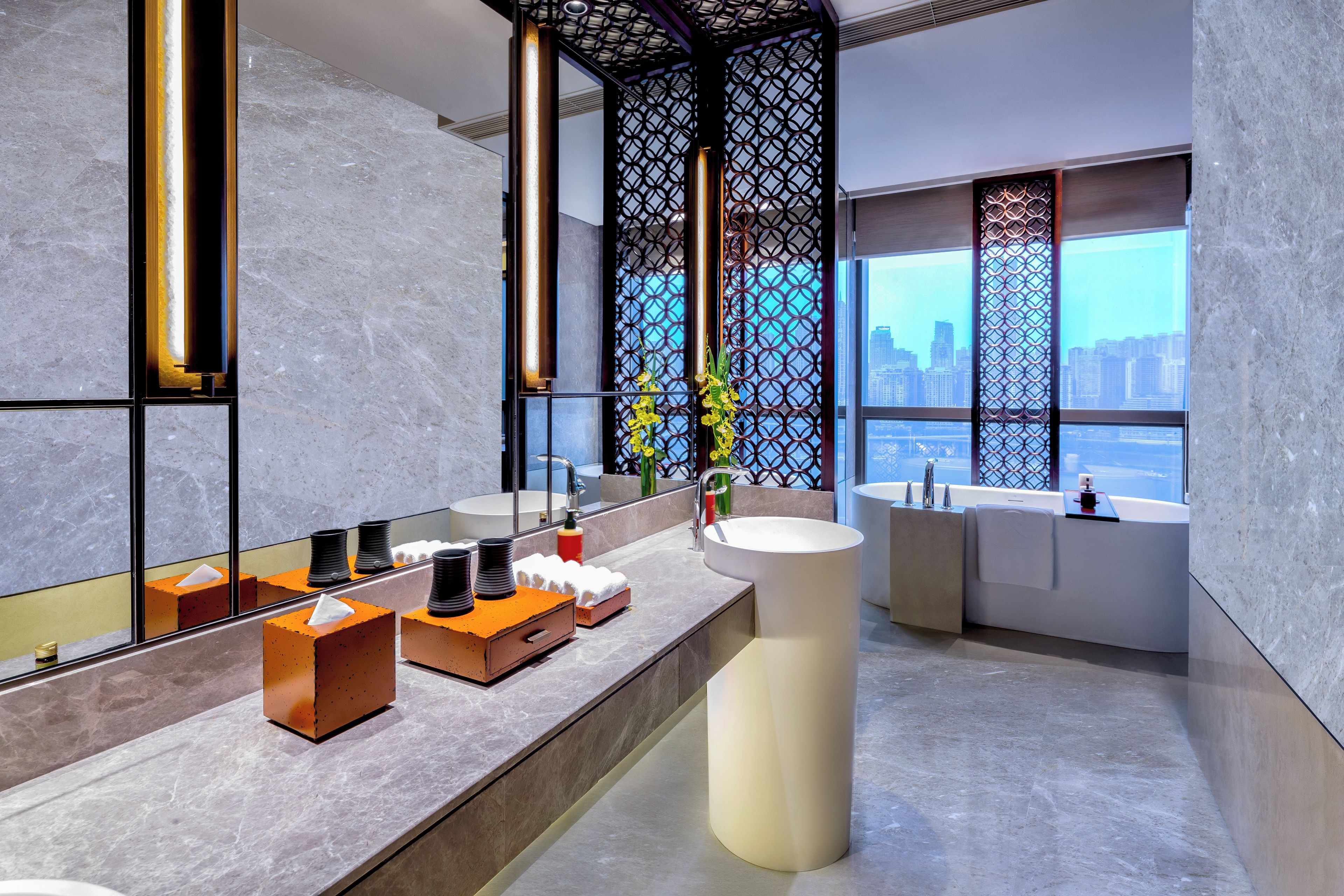 A modern bathroom with a large mirror, two sinks, a bathtub, and a city view.