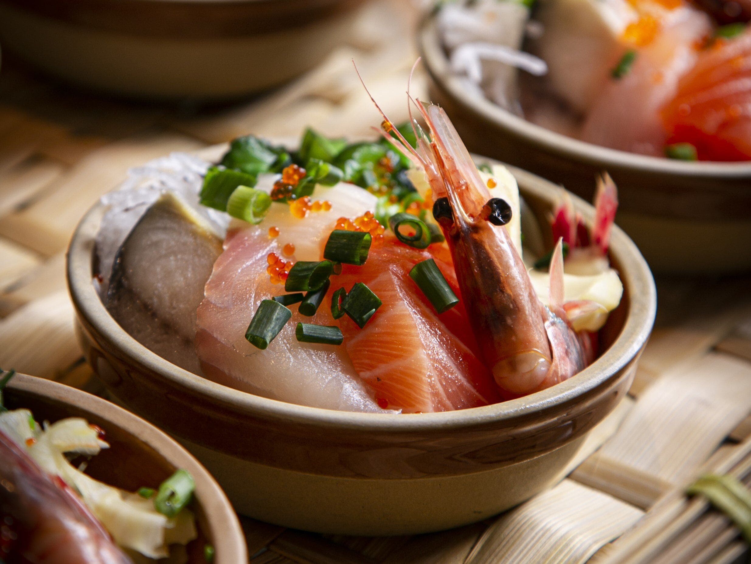 A bowl of sashimi with shrimp, salmon, and garnishes.