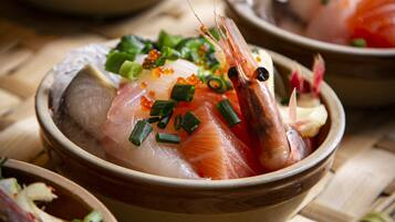 A bowl of sashimi with shrimp, salmon, and garnishes.