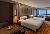 A hotel room with two beds, a dining table with fruit, a view of the city, and a patterned carpet.